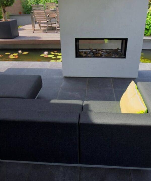 Little Island surrounded by a pond with a fireplace and a sofa in the middle on dark grey slabs
