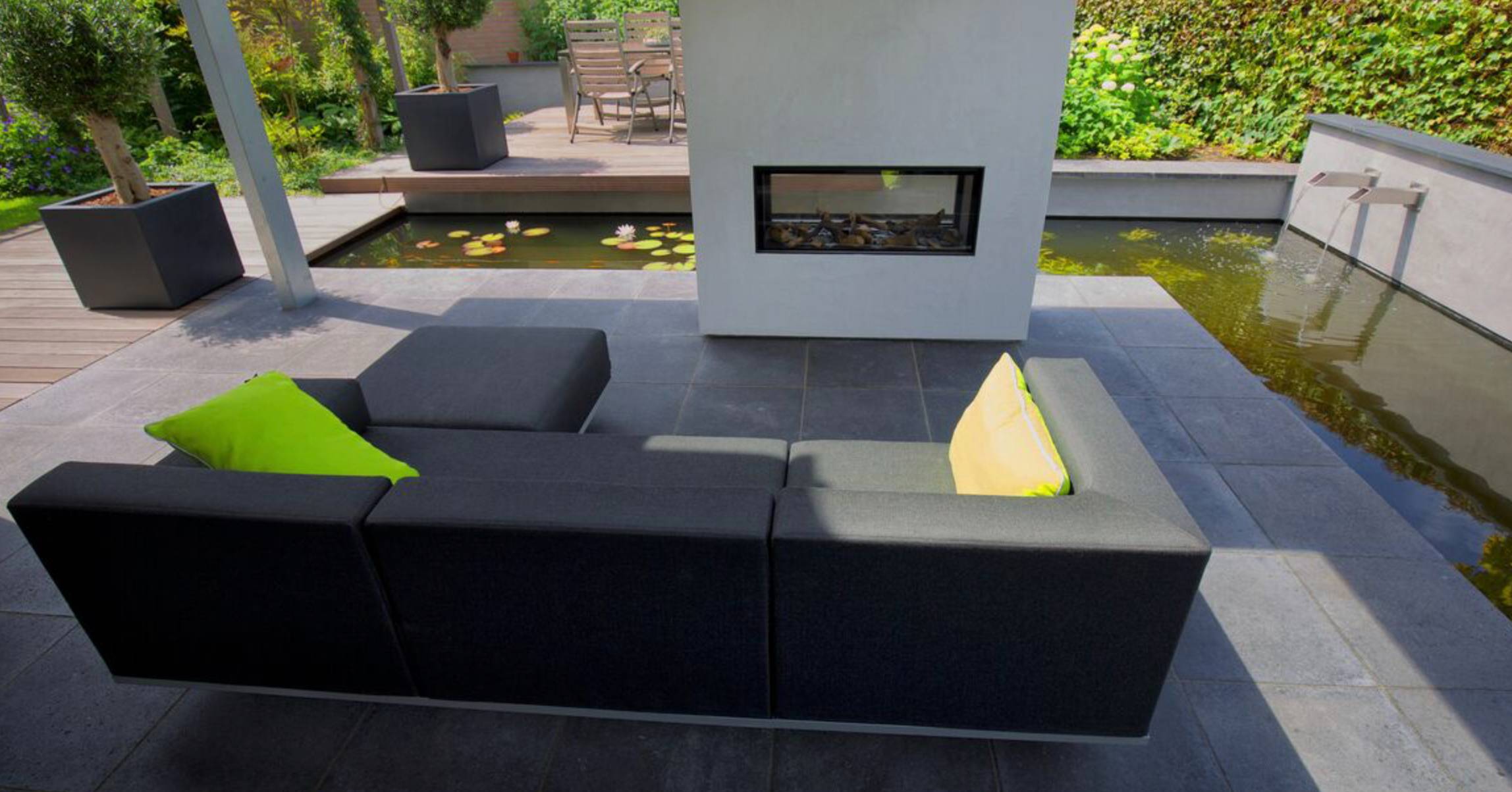 Little Island surrounded by a pond with a fireplace and a sofa in the middle on dark grey slabs