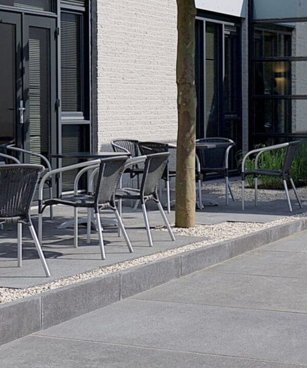 A sidewalk with a little patio next to it with tables and chairs
