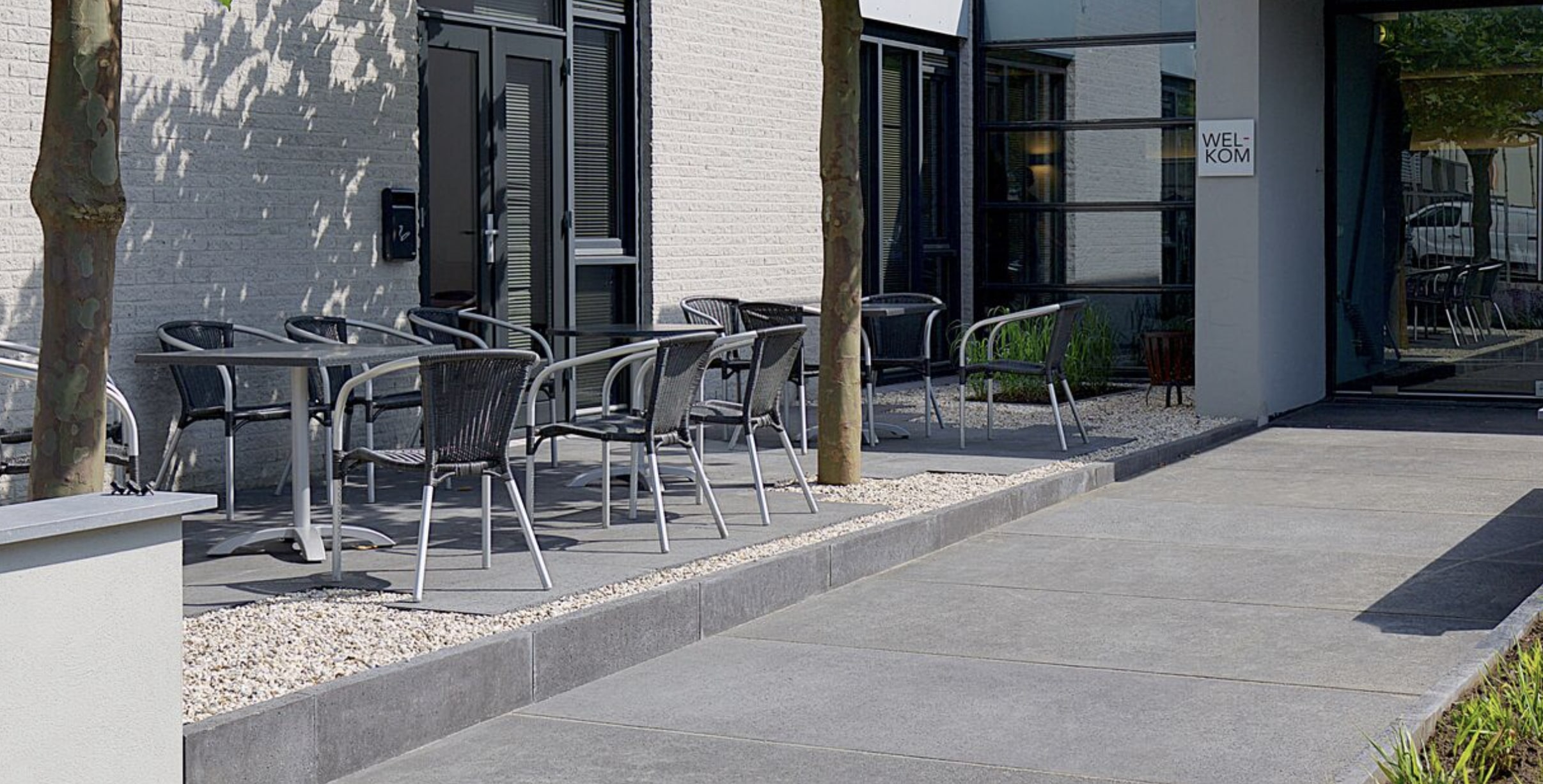 A sidewalk with a little patio next to it with tables and chairs