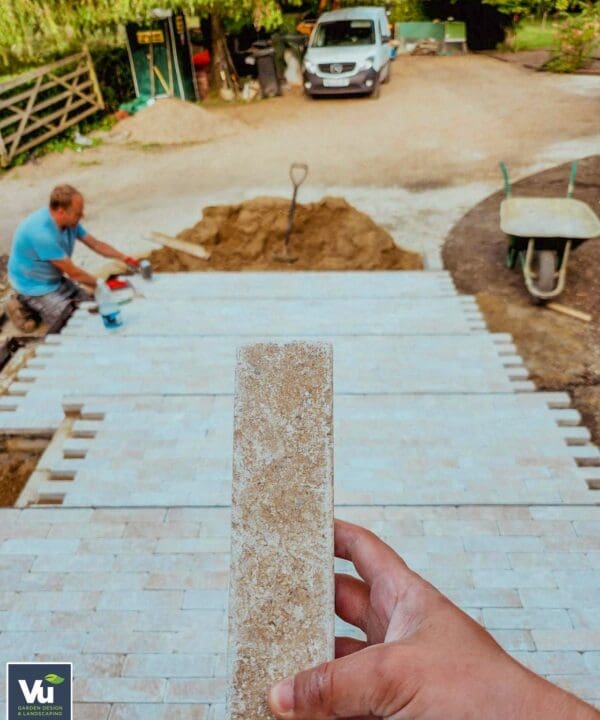A hand holding Millbrook Pearl Dual-face limestone sett with a patio being laid down in the background