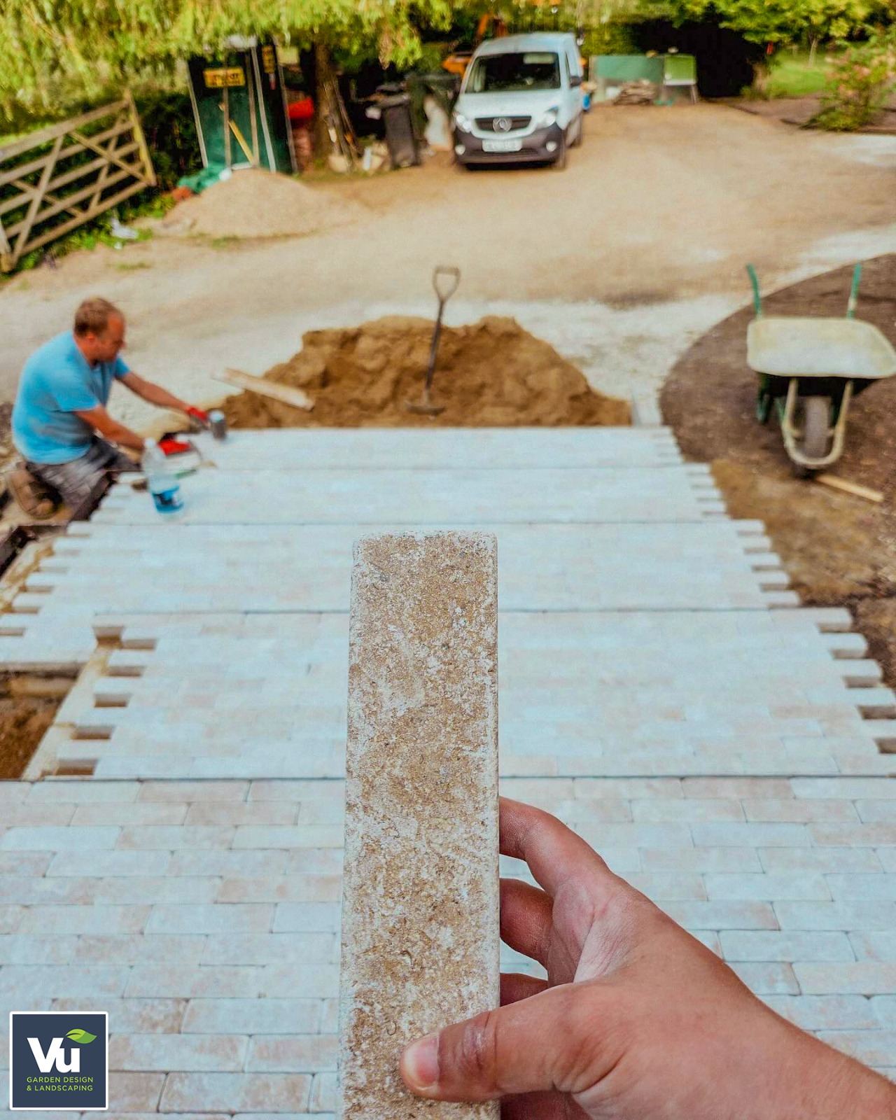 A hand holding Millbrook Pearl Dual-face limestone sett with a patio being laid down in the background